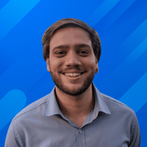 Fotografia do Consultor SEO Felipe Sawaf sorrindo, com barba e cabelo curto, vestindo uma camisa azul clara, sobre um fundo azul com um leve degradê.